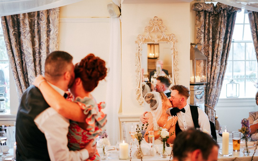 A guest couple slow dancing while the bride and groom kiss at the top table