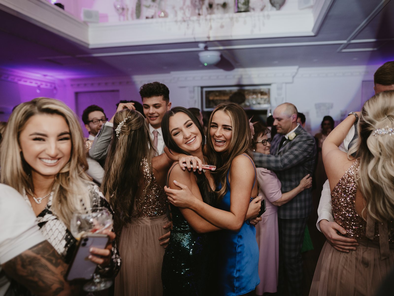 Two wedding guests hugging and laughing on a packed dance floor